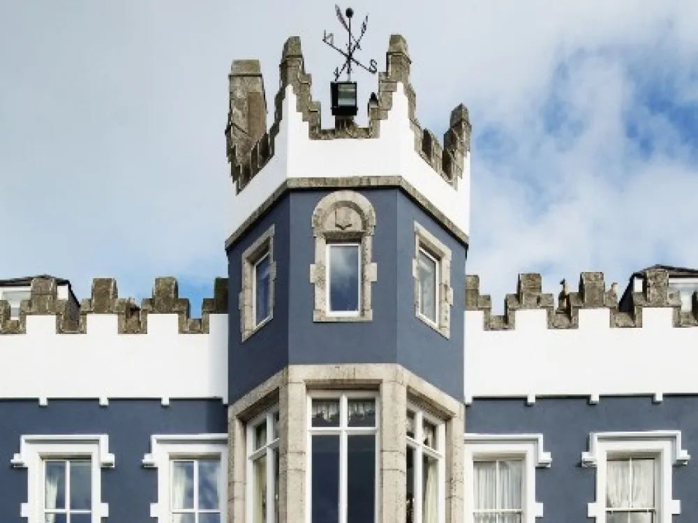 Fitzpatrick Castle Hotel with blue and white exterior, central tower featuring crenellations and a weather vane, resembling castle-style architecture