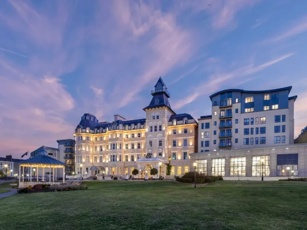 Elegant exterior of the Royal Marine Hotel at twilight with illuminated windows, central tower, gazebo, and landscaped lawn